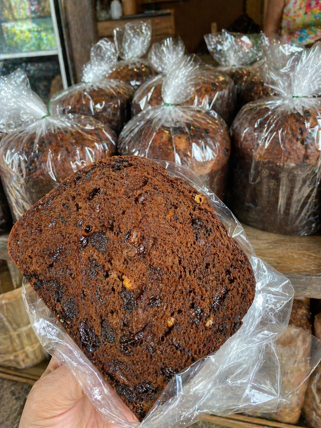 A slice of dense dark fruit bread Pan Bon held up in a bakery in Puerto Limón, Costa Rica.