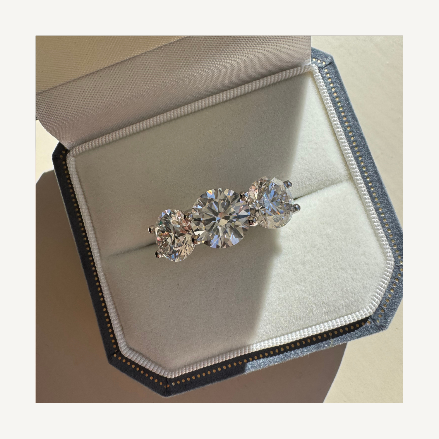 A diamond ring with three large round-cut diamonds in a jewelry box.