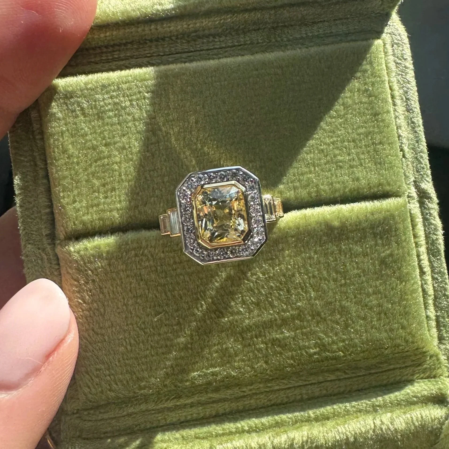 Close-up of a ring with a large yellow gemstone surrounded by smaller diamonds, displayed in a green velvet box.