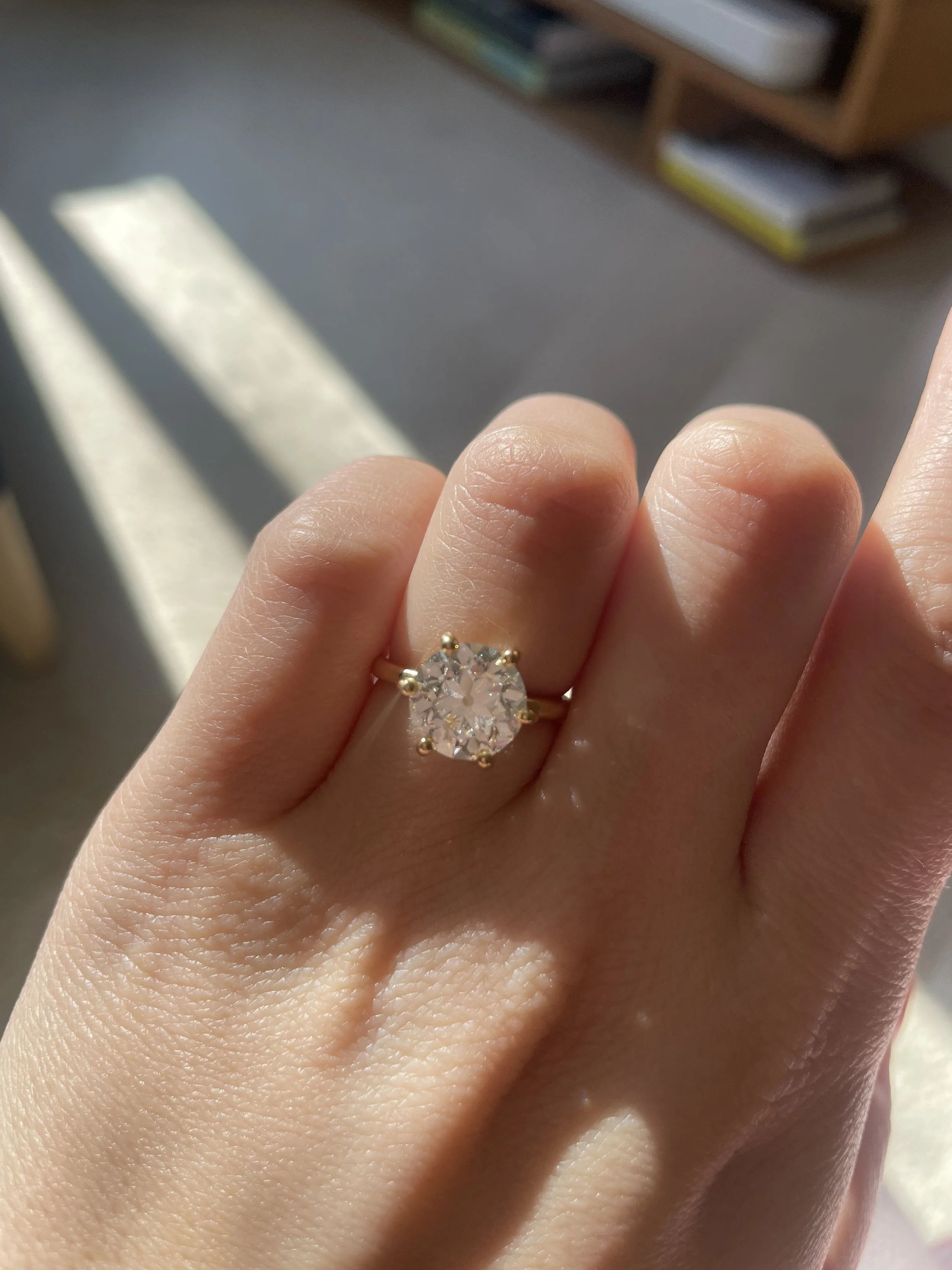 Close-up of a hand wearing a large, sparkling diamond engagement ring on the ring finger.