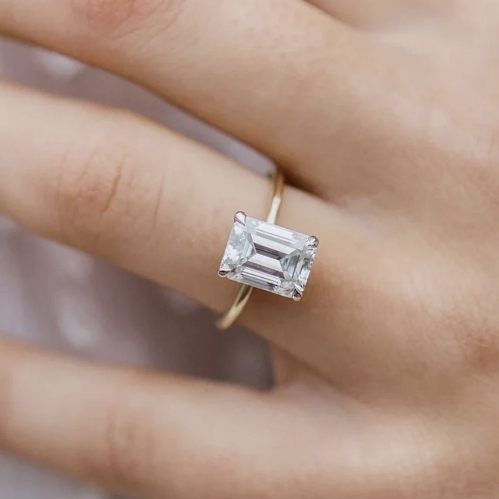 Close-up of a hand wearing a gold ring with an emerald-cut clear gemstone.