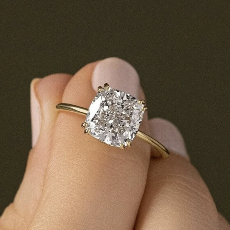 Close-up of a hand wearing a gold ring with a large square-cut diamond solitaire gemstone.