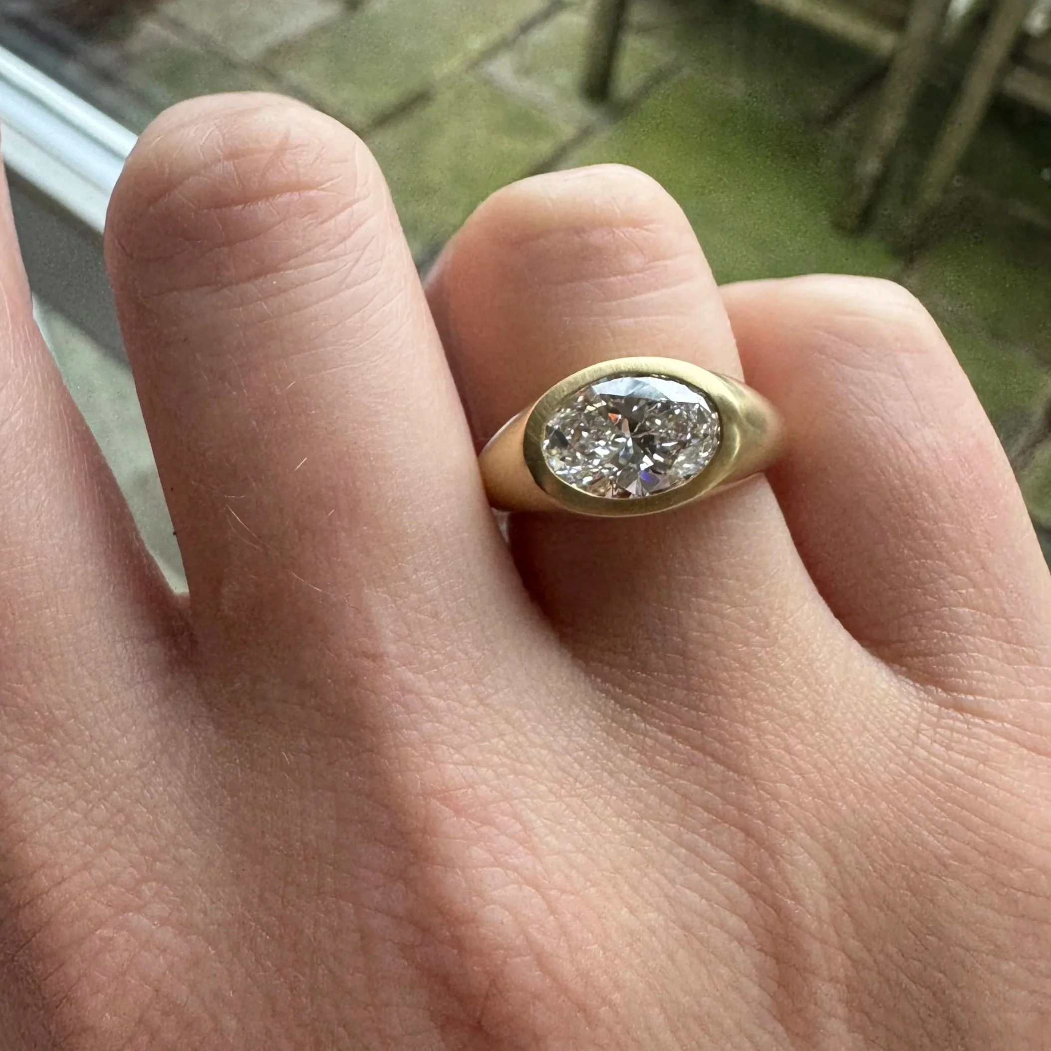 Close-up of a person's finger with a large diamond ring, showing the ring's diamond and gold band, and part of the person's hand with visible skin texture and creases.