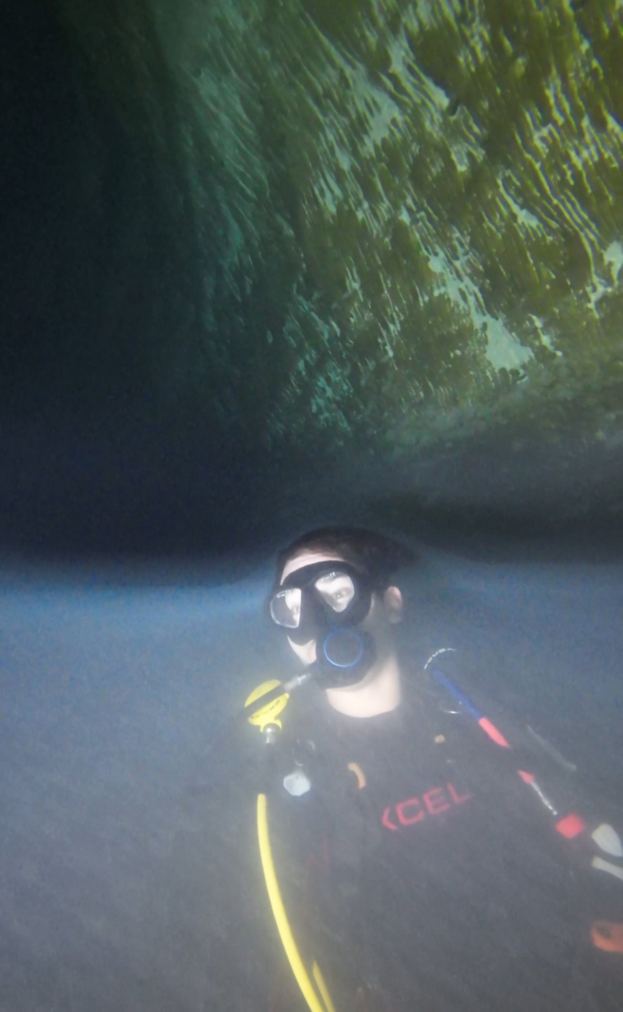 Scuba diver underwater near a rock formation with a diving mask and air regulator.