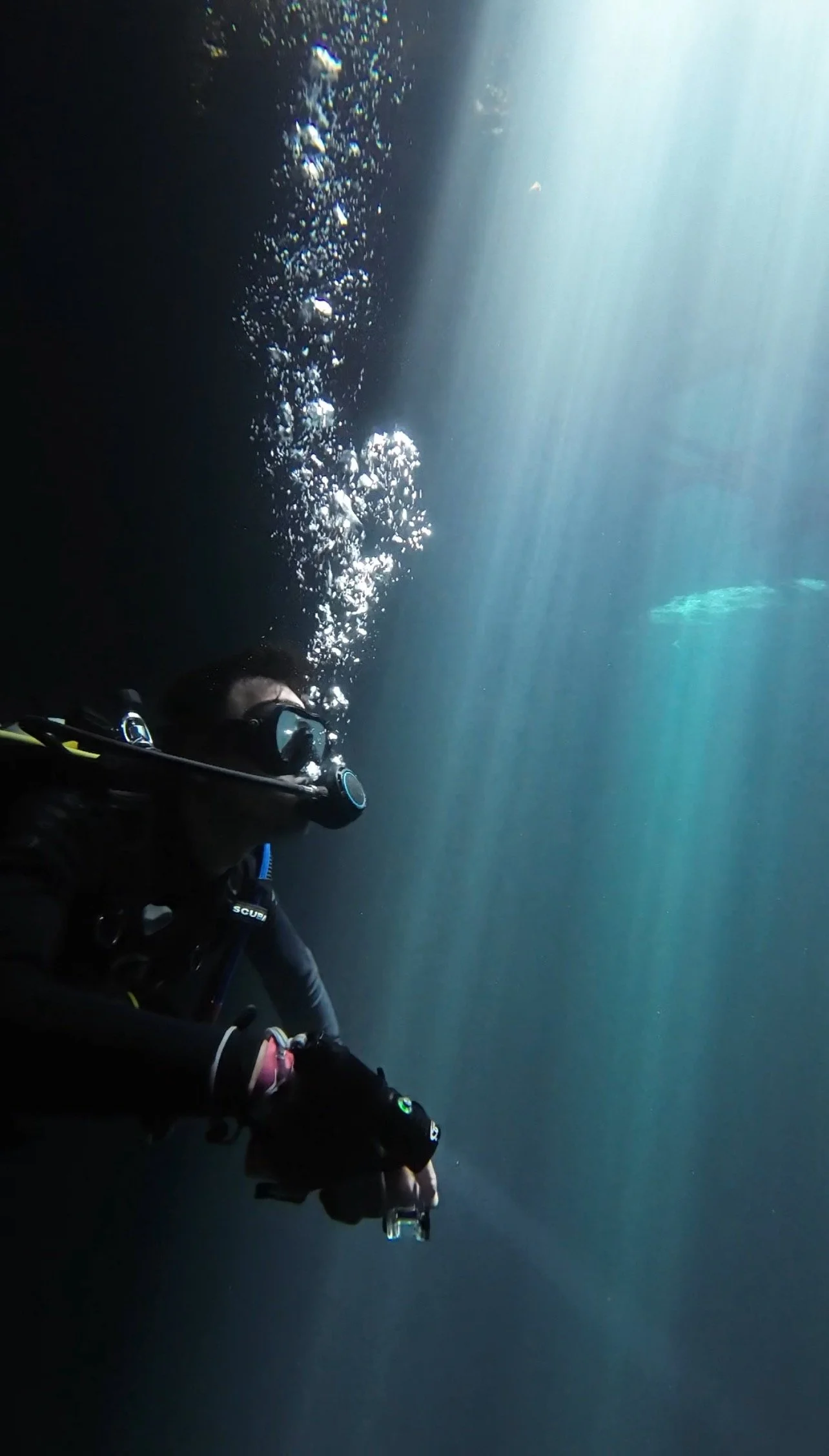 Scuba diver underwater with bubbles rising towards the surface, illuminated by shafts of sunlight.