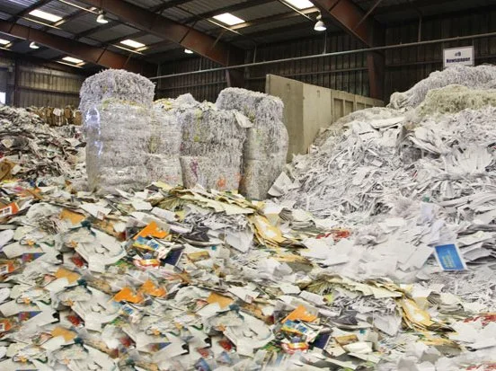 Inside a recycling facility with large piles of shredded paper and cardboard.