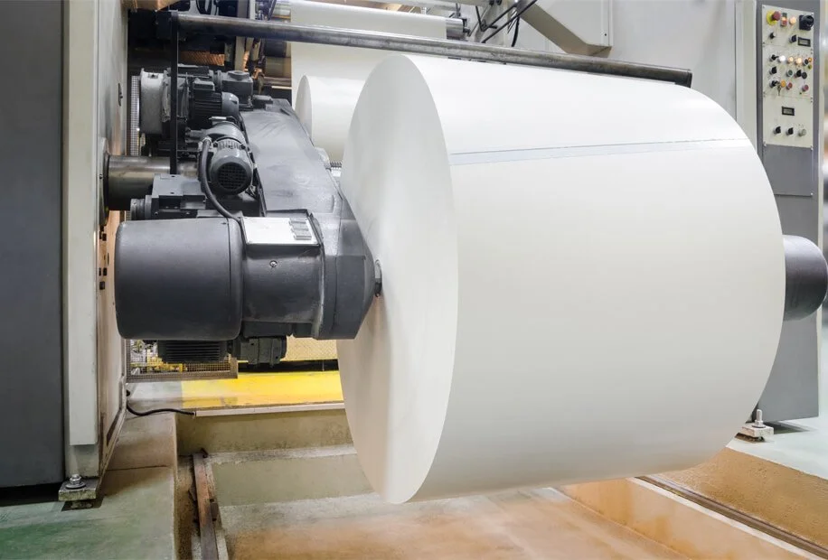 A large industrial machine unwinding a roll of white paper.