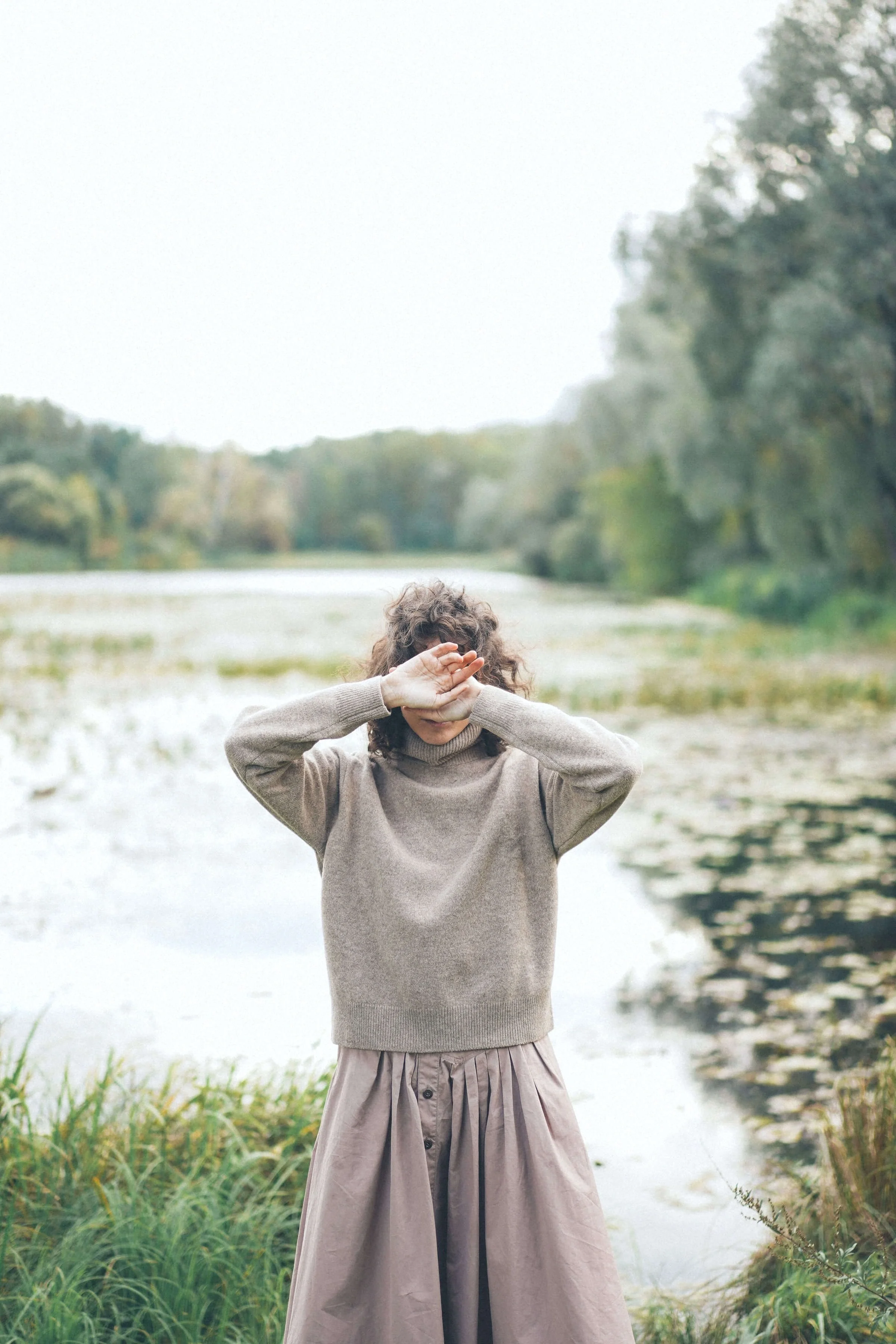 brunette woman wearing a gray sweater and covering her face with her hands