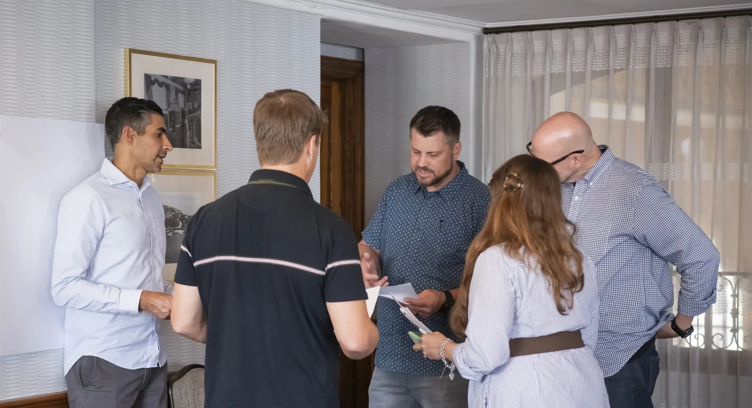 Five Excelerate consultants standing together, reviewing printed materials during a working session.