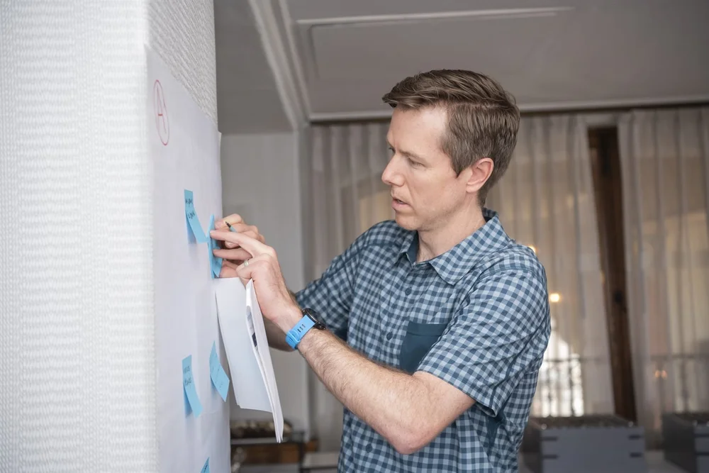 An Excelerate consultant placing sticky notes on a wall during a working session.