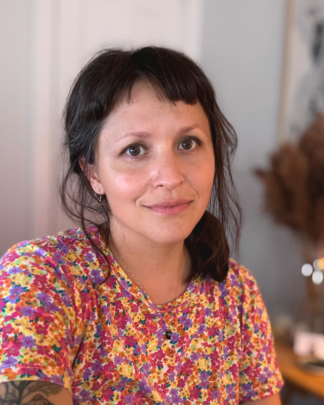 A woman with short dark hair wearing a colorful floral shirt, smiling indoors.