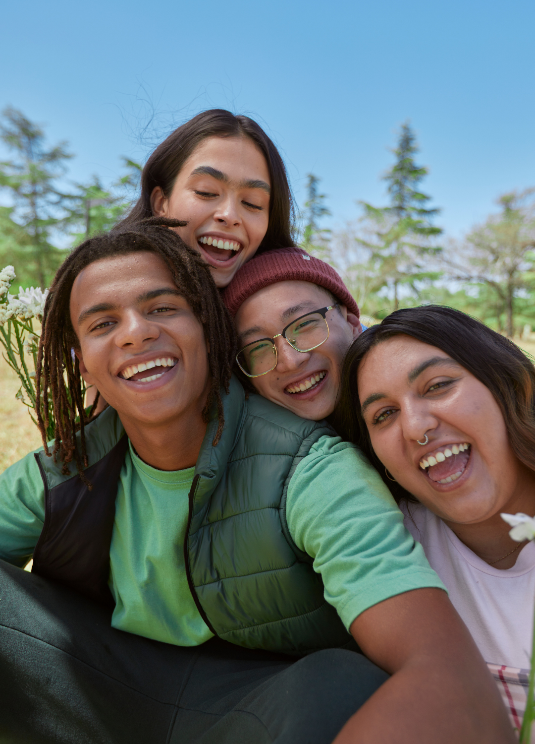 Group of five diverse friends taking a selfie outdoors on a sunny day, smiling and close together.