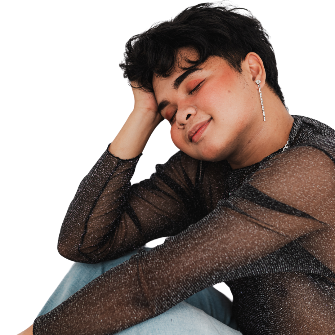 A person with short dark hair and makeup, wearing a sparkly black top and a long earring, is resting their head on their hand with a gentle smile.