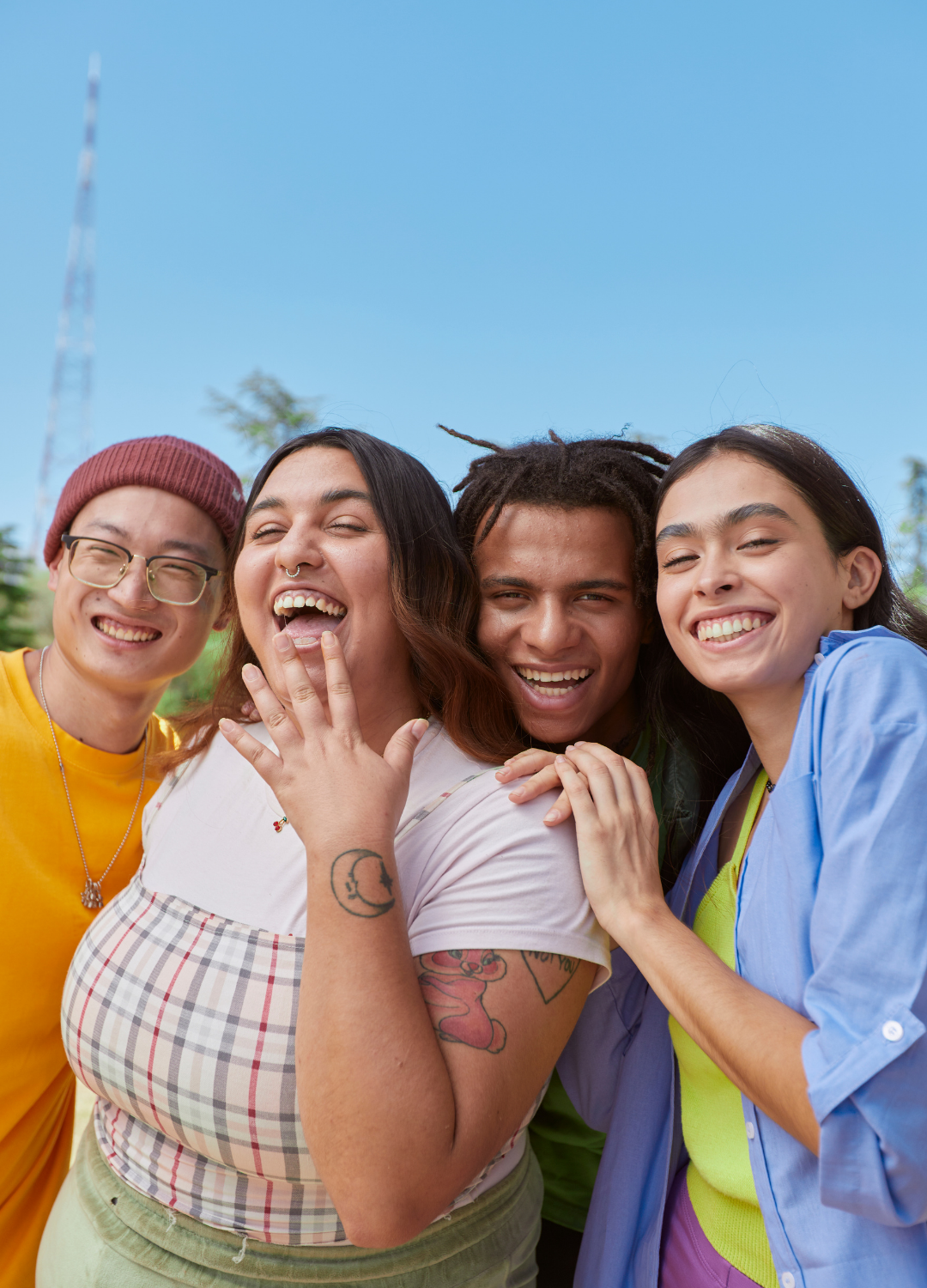 A group of four diverse young adults smiling and laughing outdoors on a sunny day.