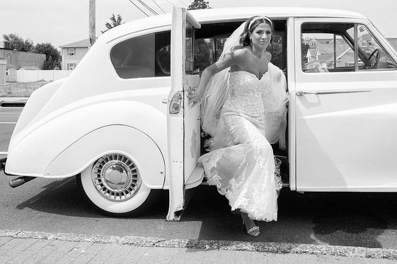 Bride in wedding dress getting out of vintage white car