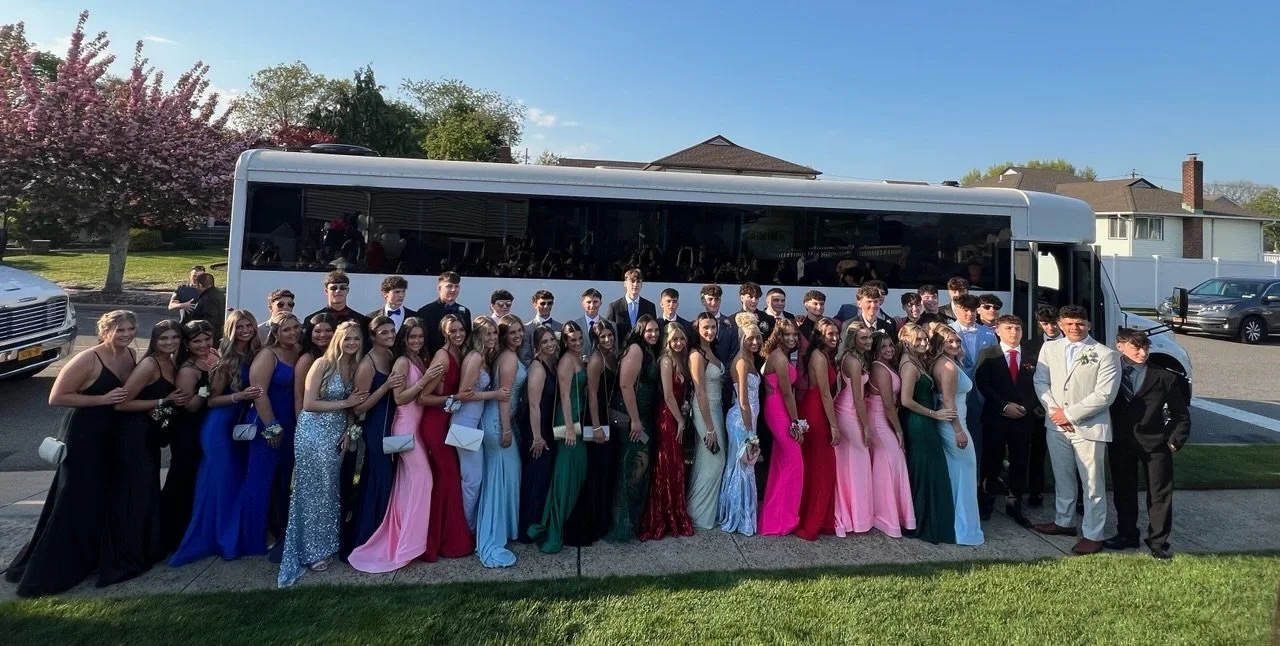 A large group of young people dressed in formal attire outside, posing for a photo in front of a bus.