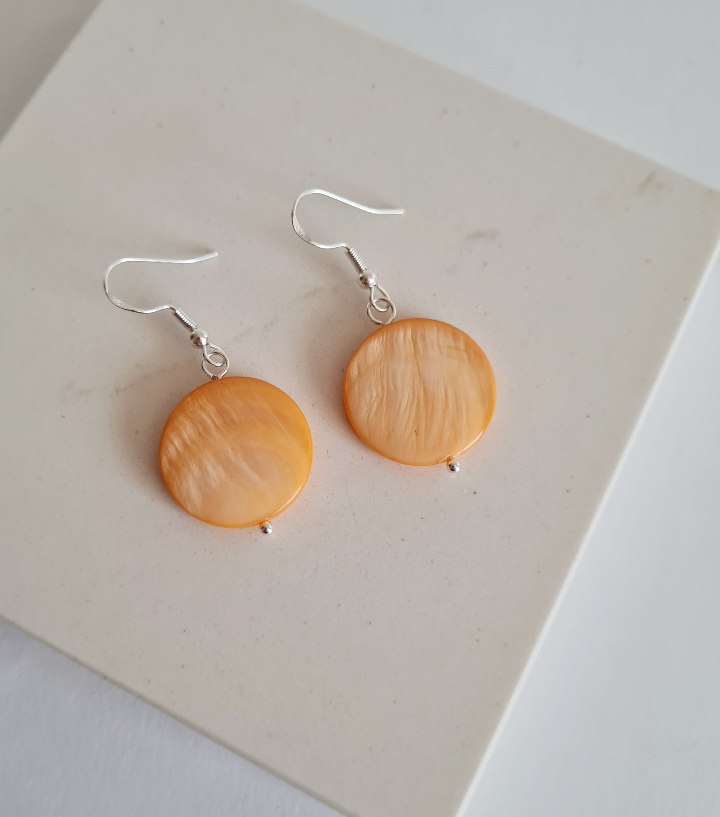 Handmade orange shell disc earrings on sterling silver wire hooks.
