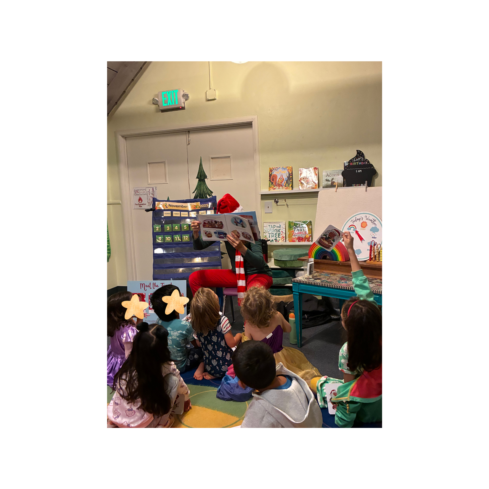 Ellen H.S. reads Merry Claus and the Holiday Dash to a group of students. She is wearing red pants and a striped scarf. The book covers her face.