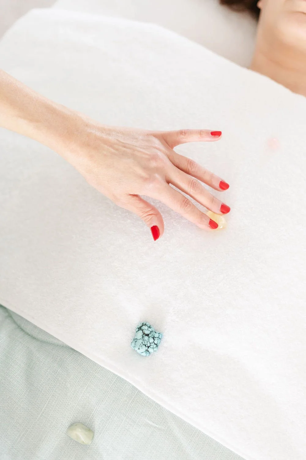 A person with red painted nails touches a white surface with a cracked blue stone or mineral stone on it.