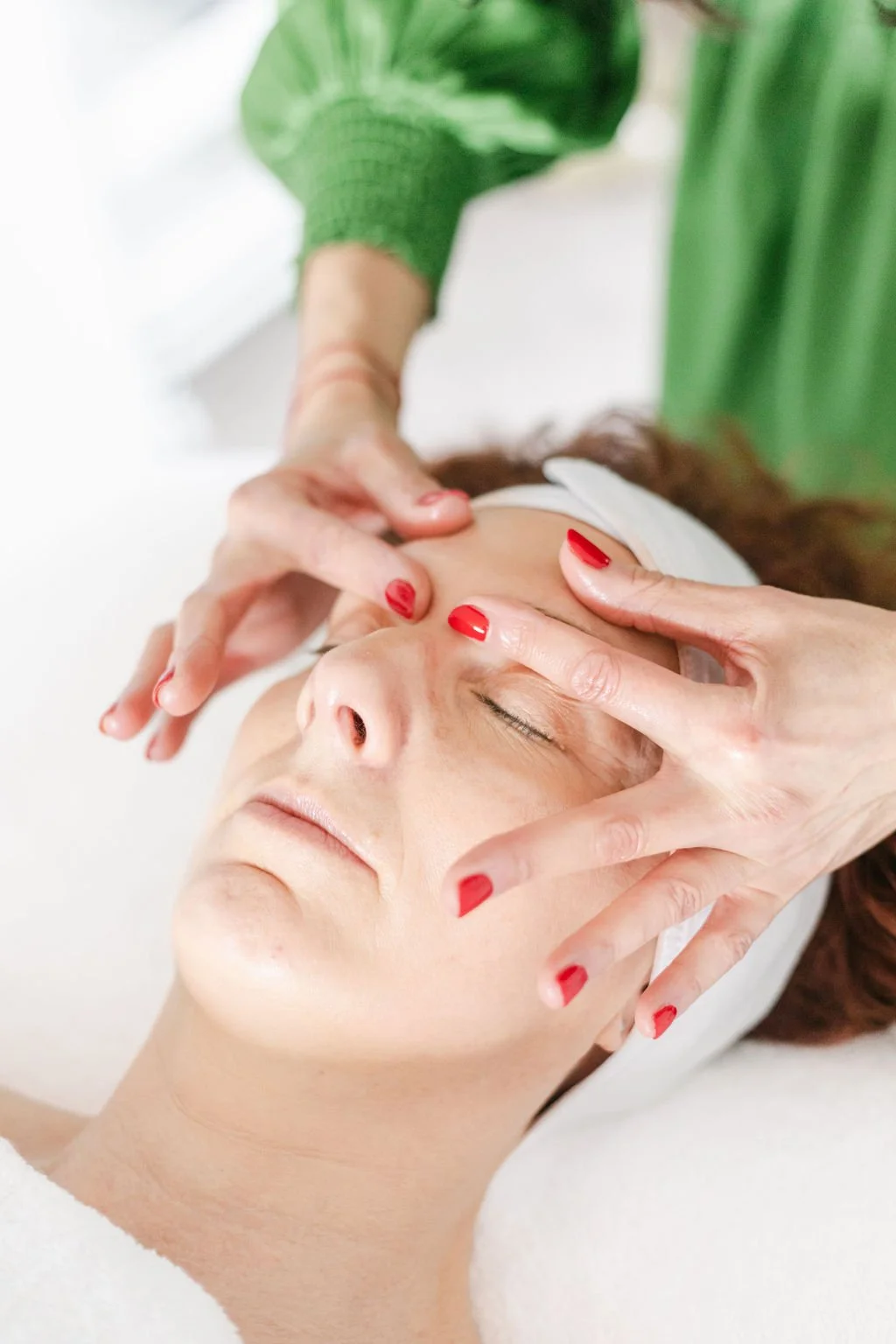 A woman receiving a facial massage from a therapist