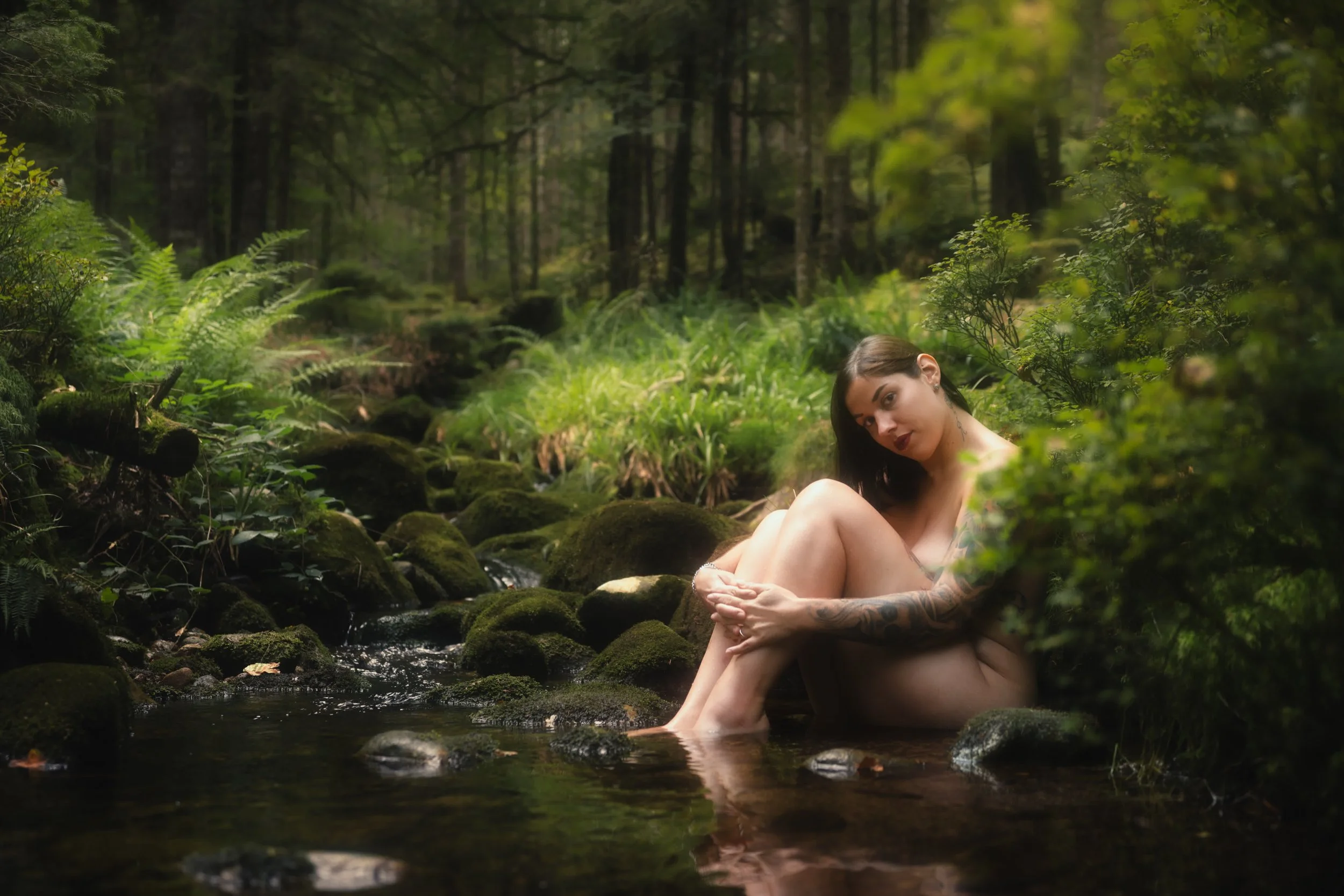 Photoshoot doux d'une femme nue assise dans une petite rivière dans une forêt verte.