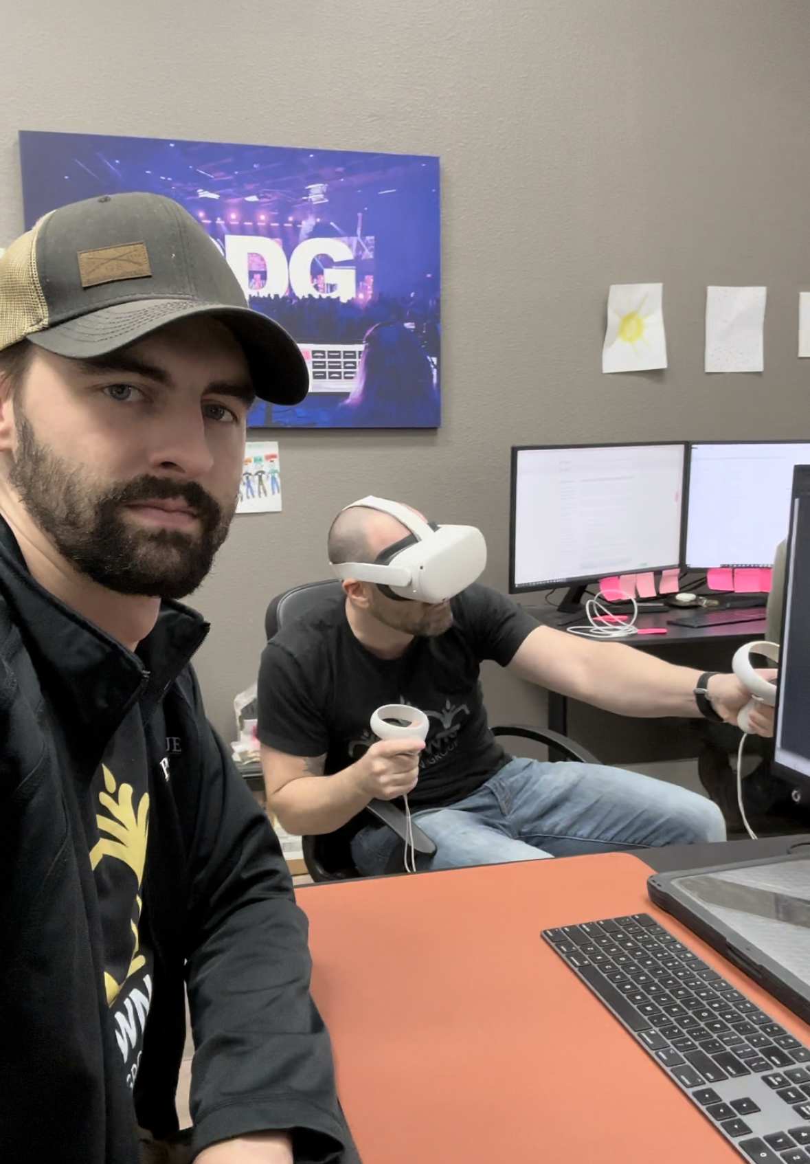 Luke Wheat and Garrett Walker in an office, Garrett using VR headset and controllers, computers on desk.
