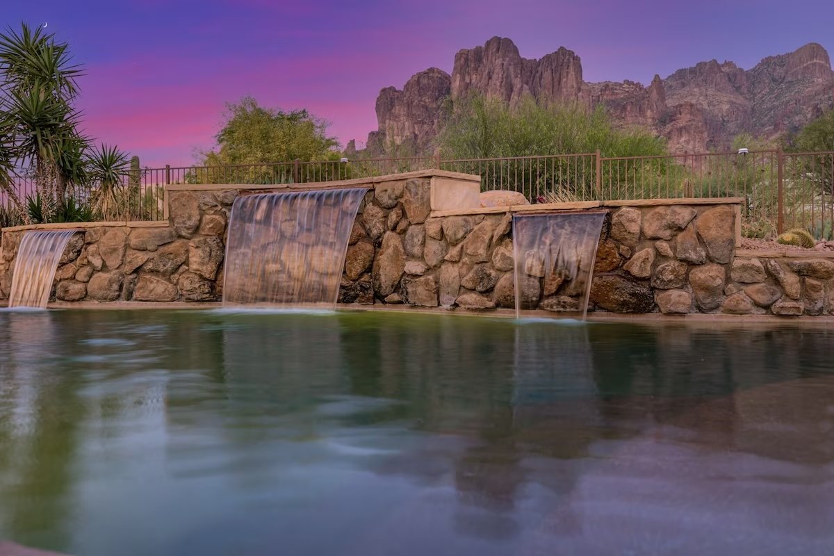 Rock waterfall into a pool with desert landscape and mountains at sunset.