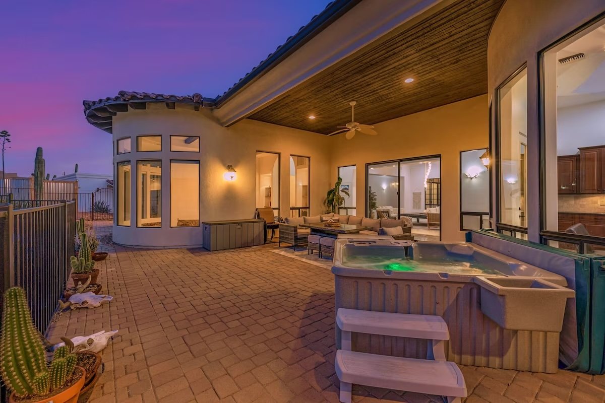 Outdoor patio at dusk with seating area, hot tub, potted cacti, and modern house exterior.