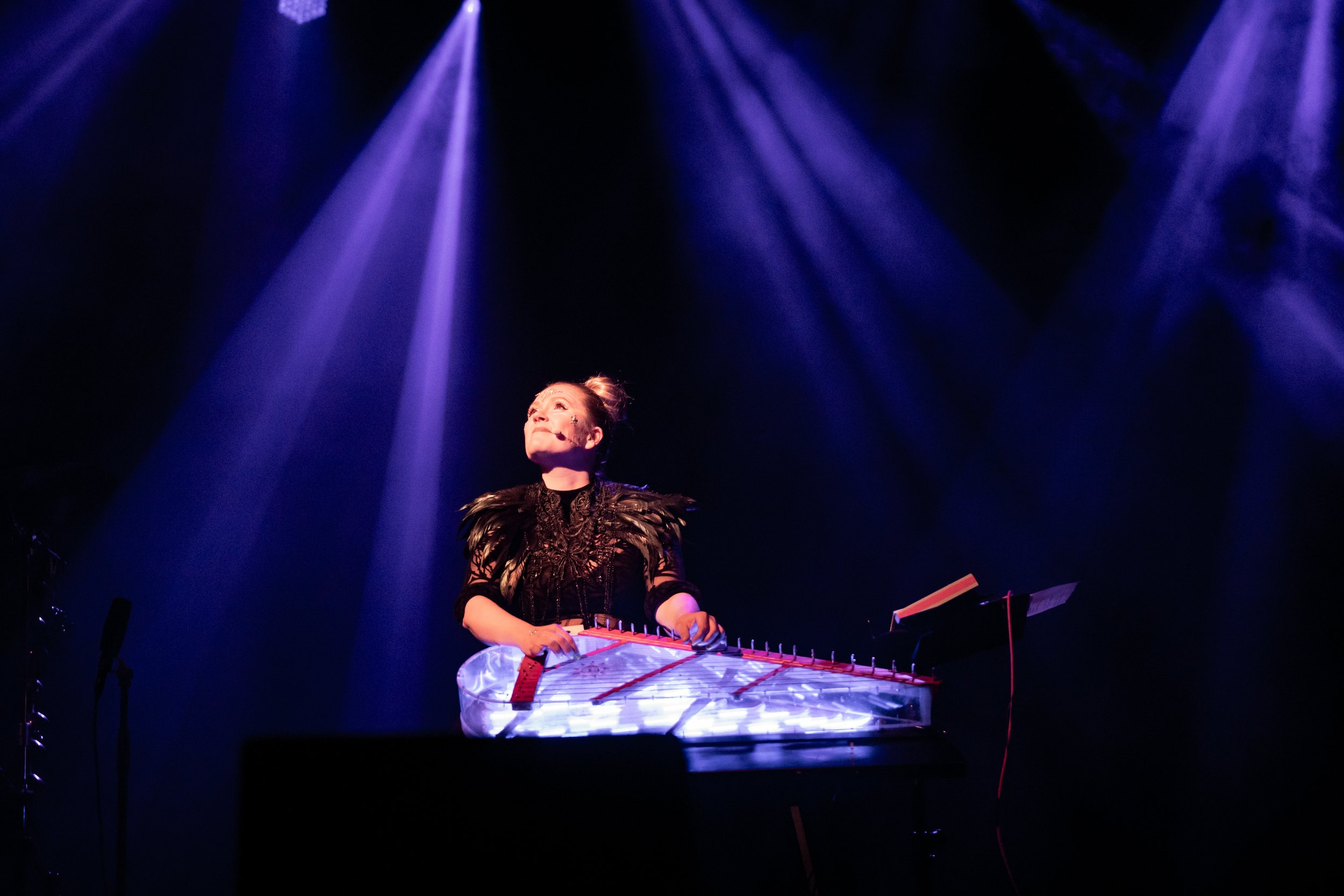 Press photo of Maija Kauhanen. A woman on stage playing a kantele illuminated by purple spotlights.