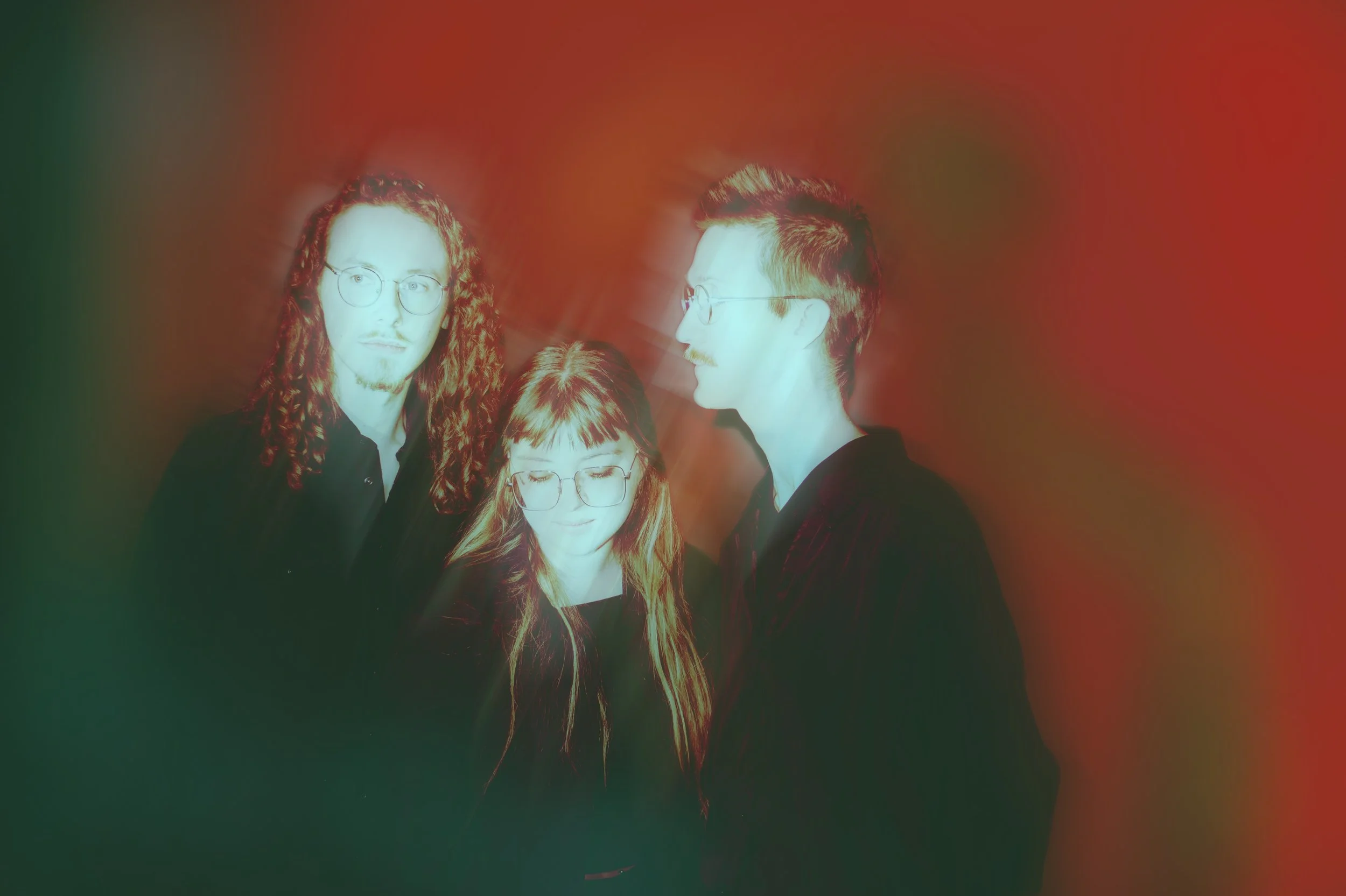 Pres photo of Kalejdoskop Trio. Three people with glasses standing close together against a colorful background.