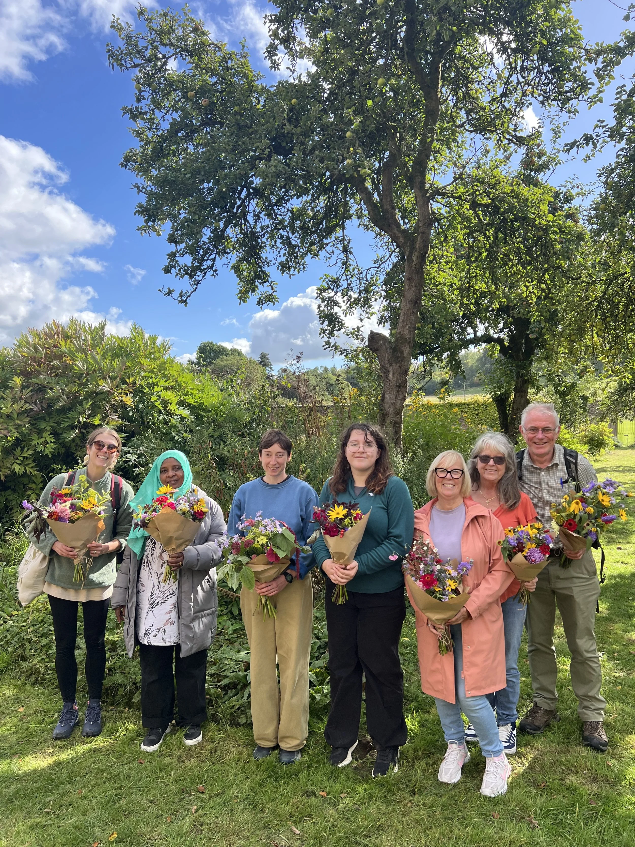 A group of women stand in the walled garden holding bouquets.