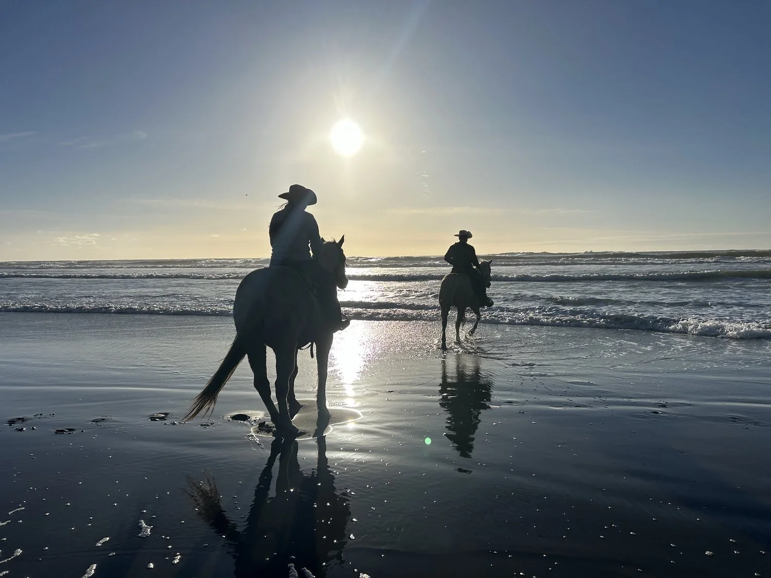 Two riders in the surf at sunset, backlit