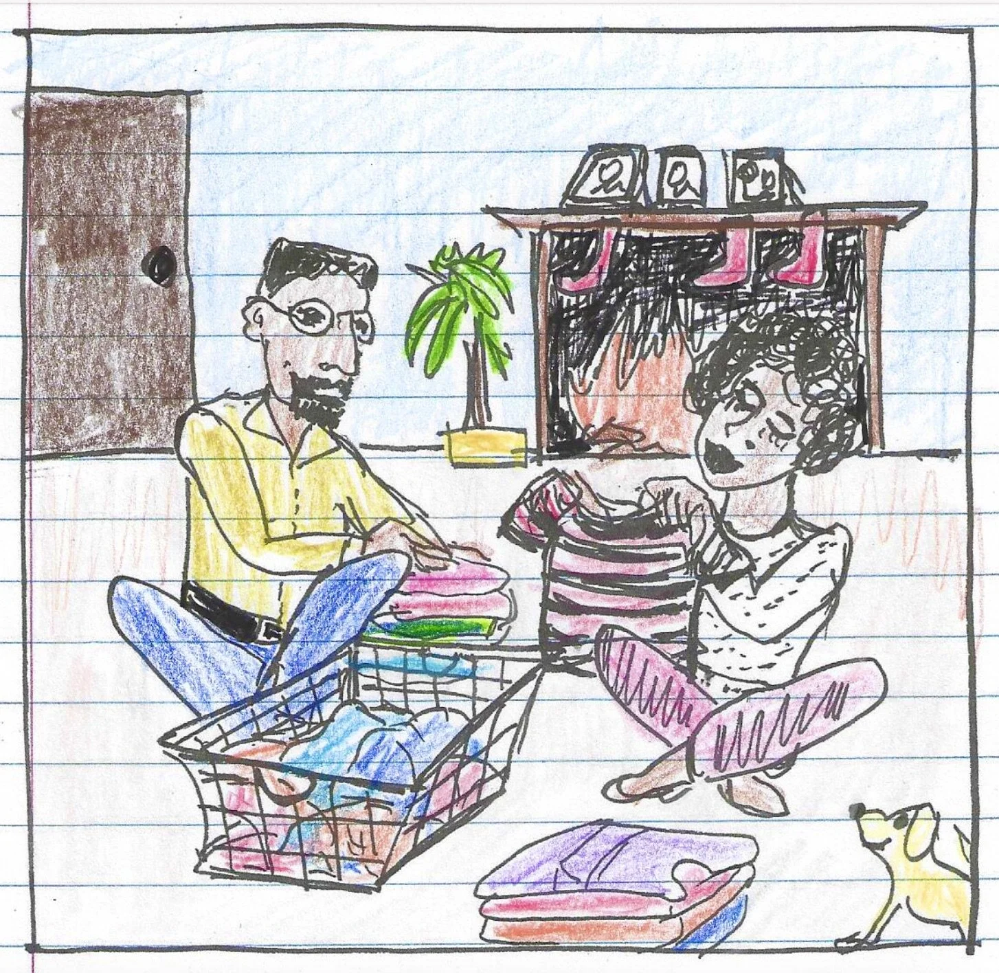 A man with dark, curly hair and a beard wearing clear glasses and a dark green sweater, sitting indoors with a neutral background and a plant in the distance.