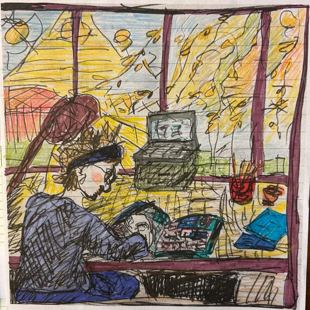 A man with dark curly hair, glasses, and a beard, sitting indoors with a neutral expression, wearing a dark green sweater, and a plain white shirt underneath. A plant is visible in the background.