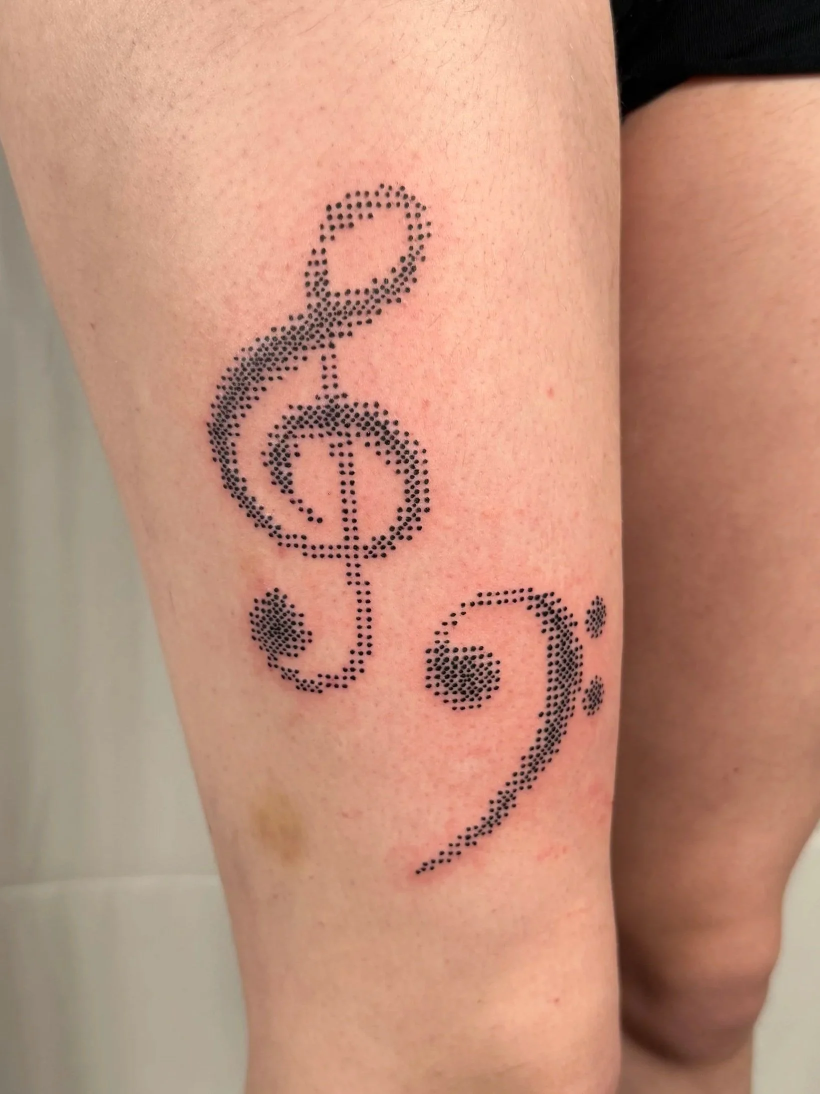 Tattoo of a musical treble clef symbol made of tiny black dots on a person's leg.