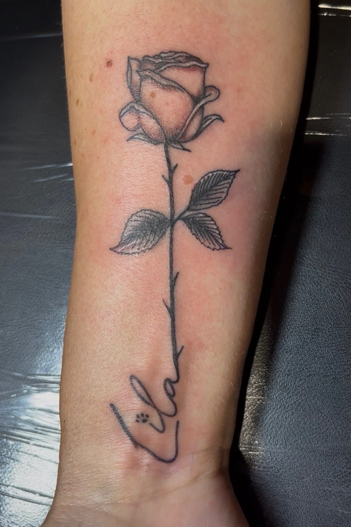 Tattoo of a rose with detailed leaves, with the word 'Love' written in cursive script below it.