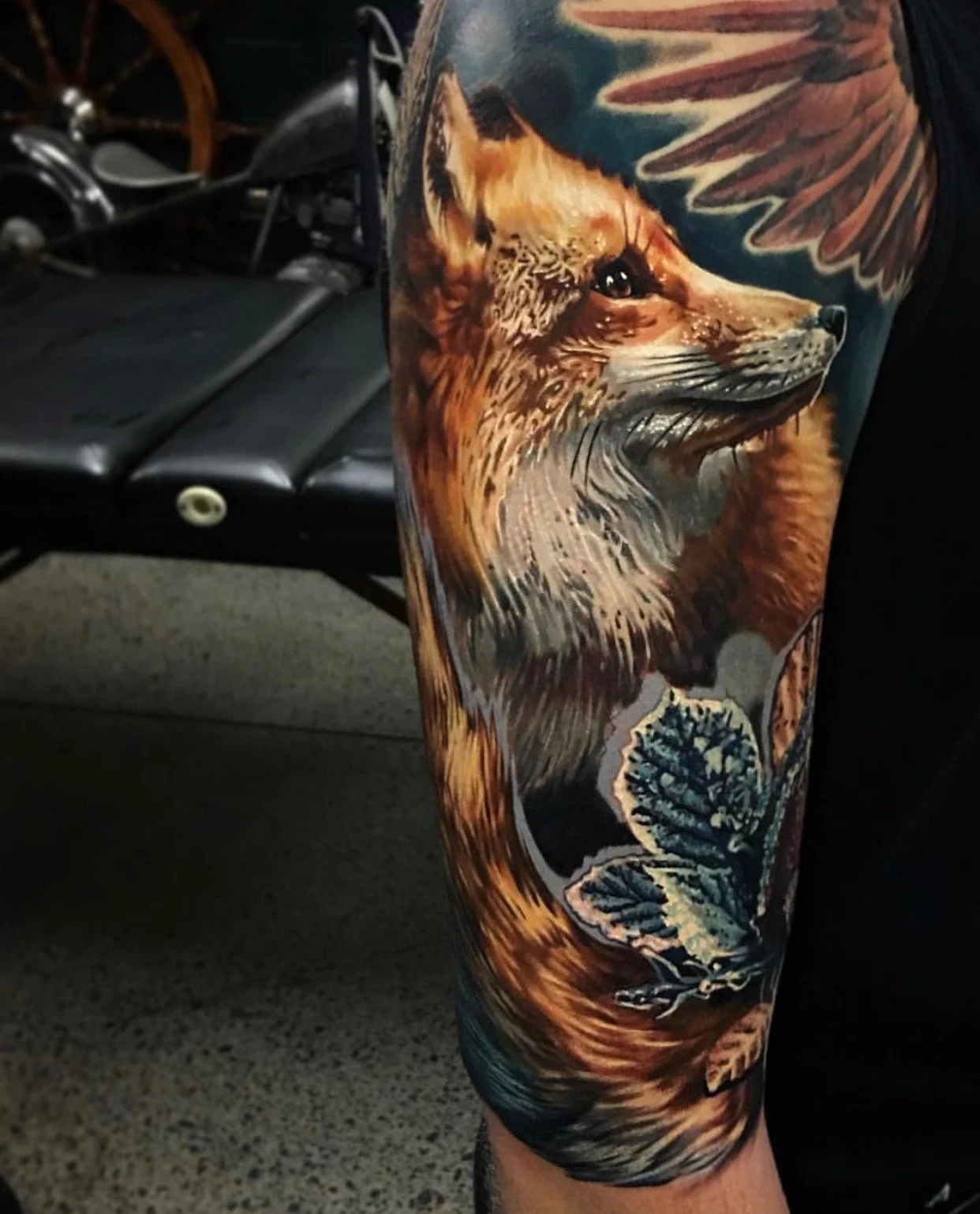 Tattoo of a fox's face, leaves, and feathers on a person's arm.