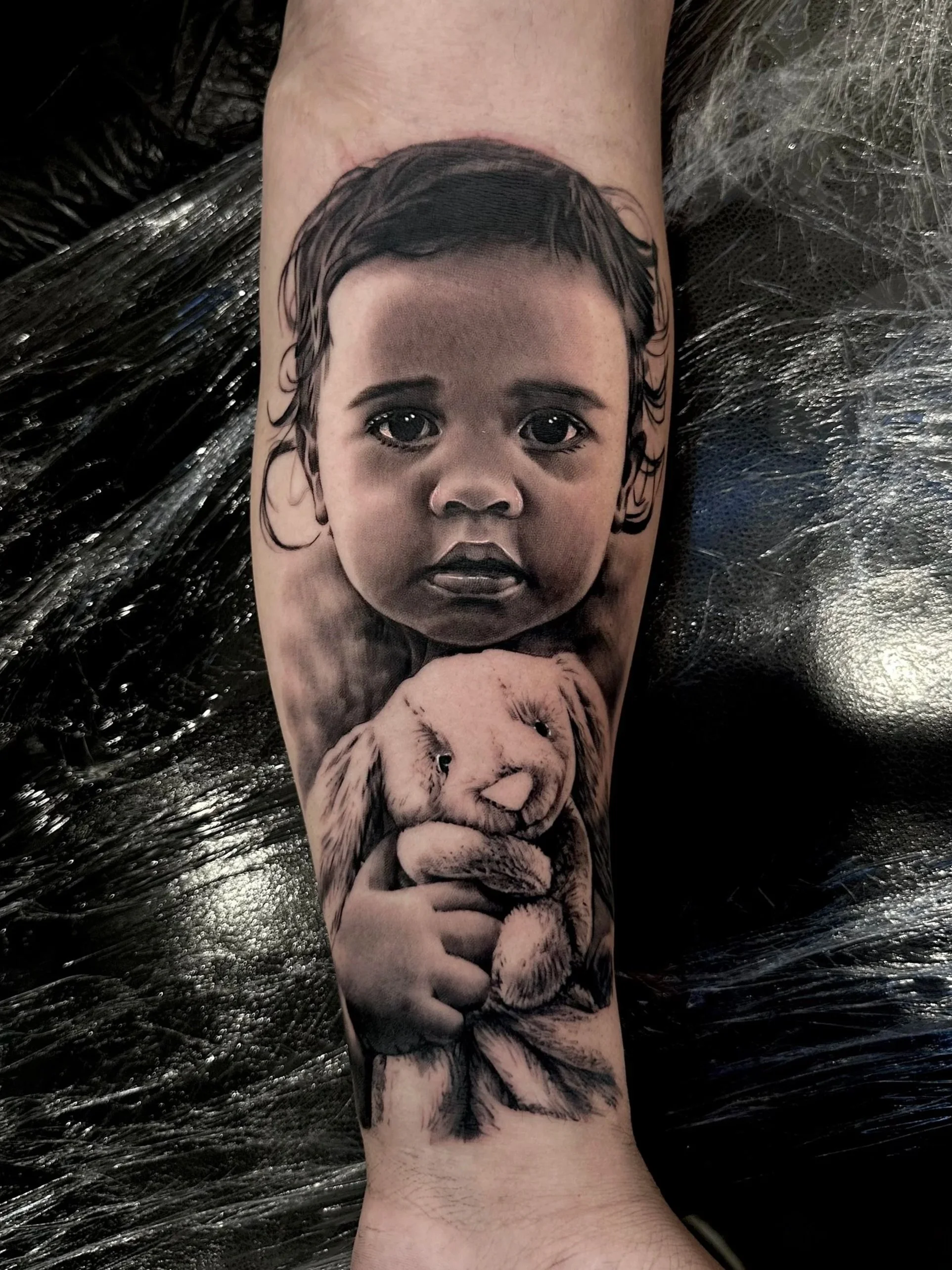 Tattoo of a realistic child girl’s face holding a lion cub on a person’s leg.