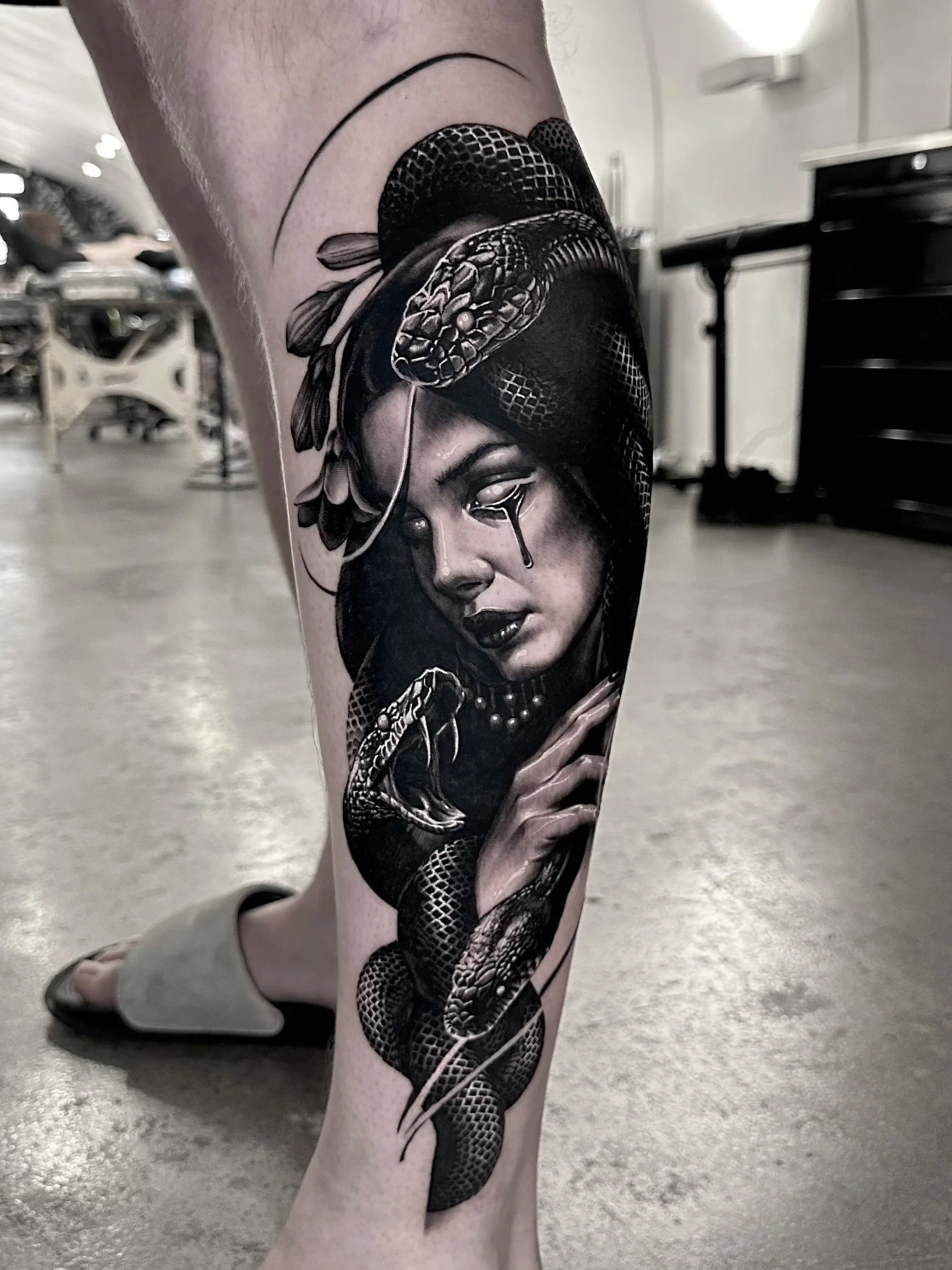 Tattoo of a woman's face with snakes and a snake slithering down her leg on a person's thigh.