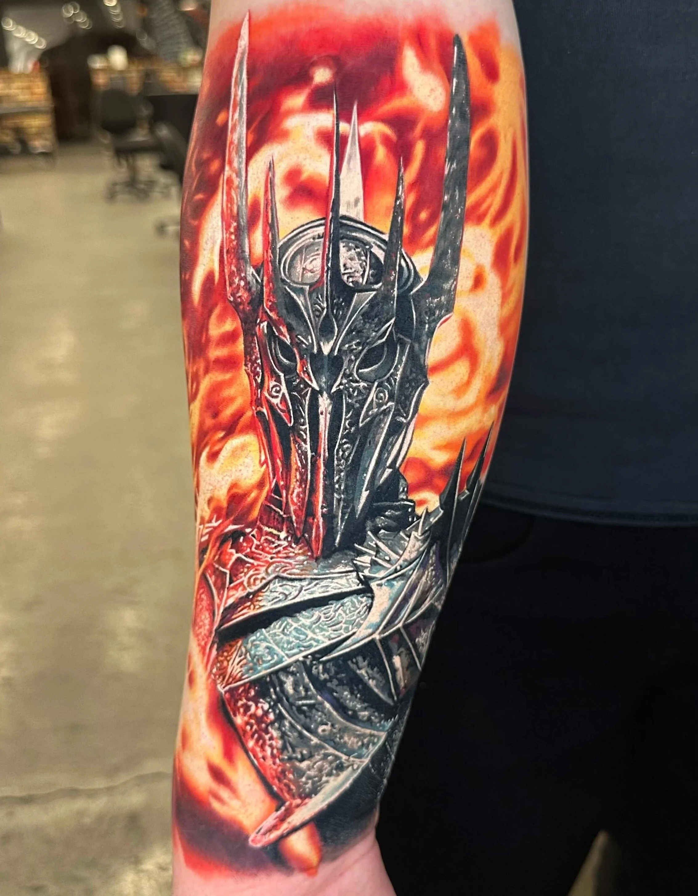 Tattoo on an arm depicting a detailed metallic dragon sword with flames in the background.
