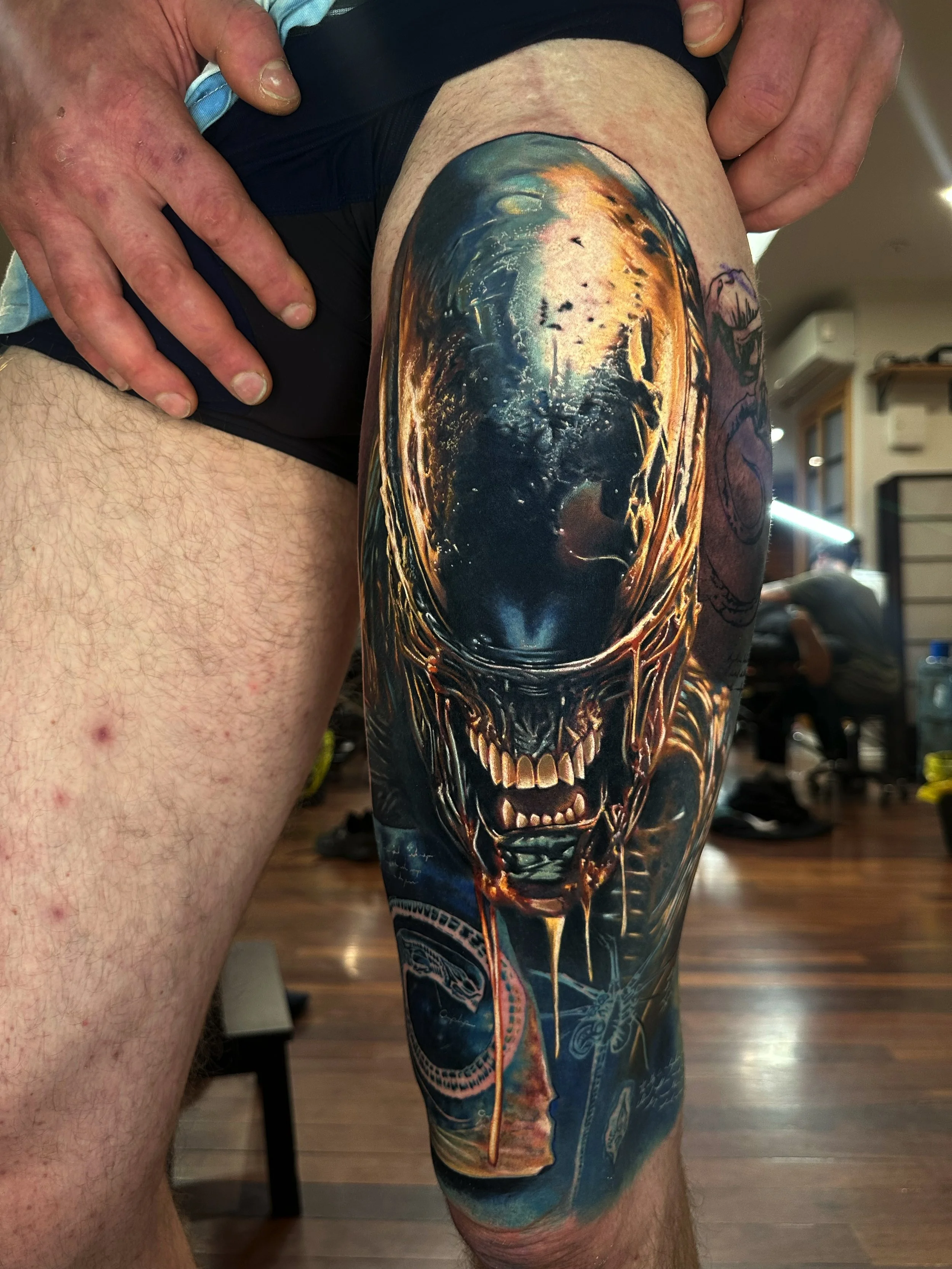 A photograph of a person's thigh with a colorful, detailed tattoo depicting a skull with dark eye sockets and a dramatic, fiery background.