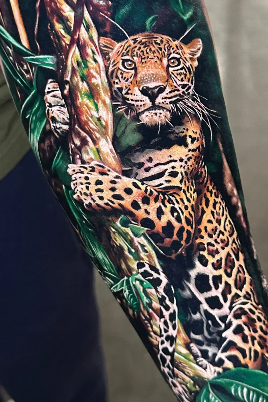 Photograph of a tattoo of a jaguar in a jungle setting with green leaves and tree branches.