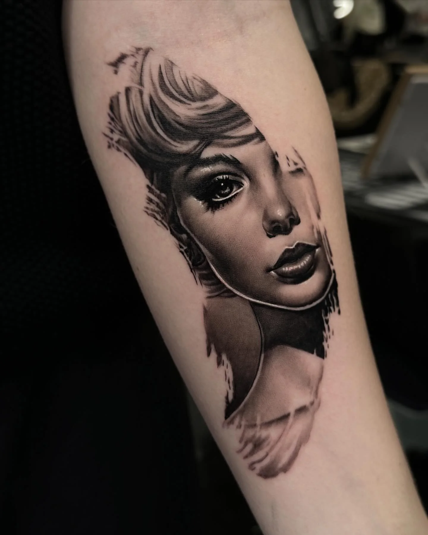 Black and gray tattoo of a woman's face with short hair on a person's arm.