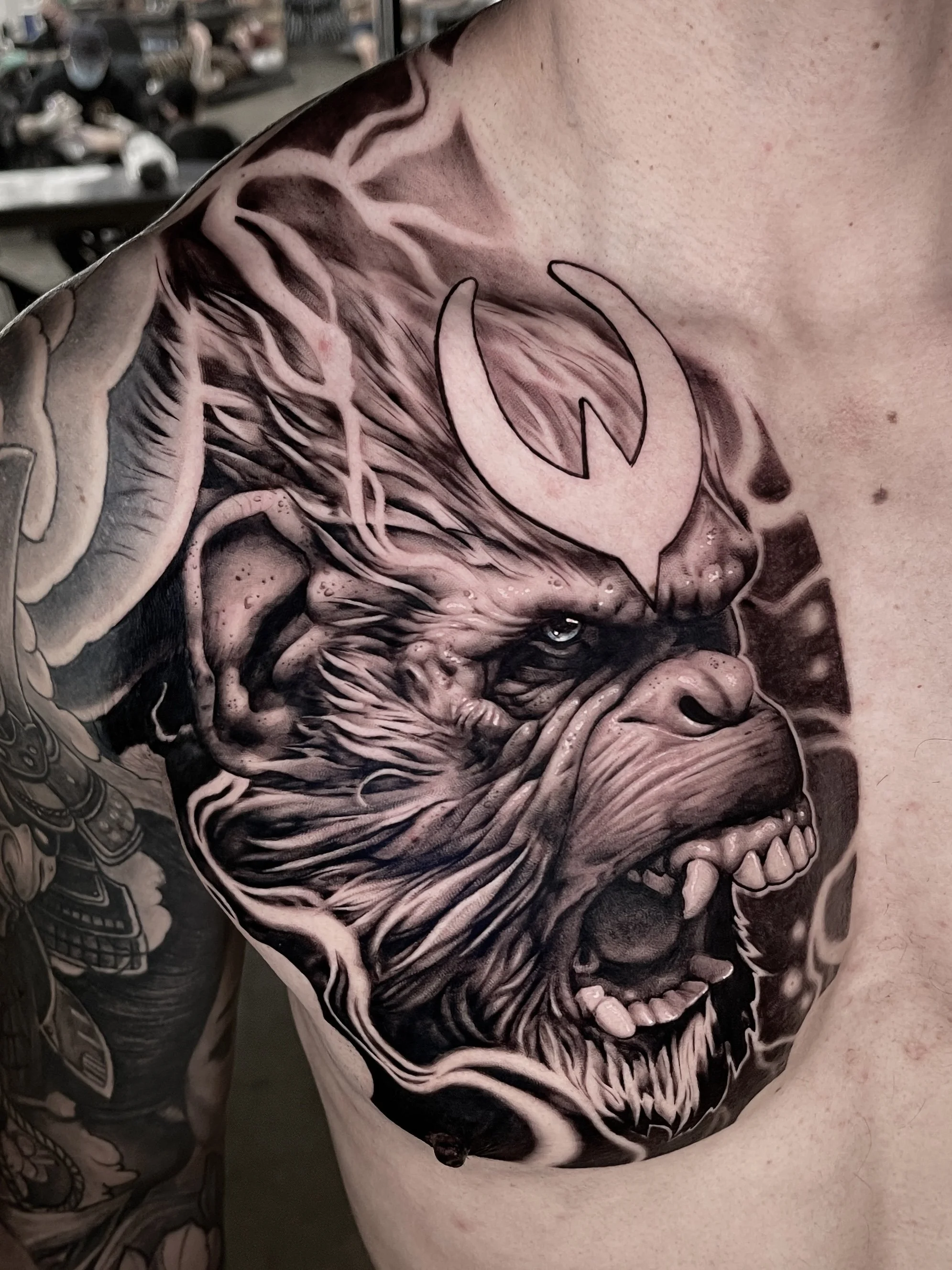 Close-up of a black and gray tattoo of a fierce wolf with bared teeth, intricate fur details, and a speech bubble with a stylized leaf inside.