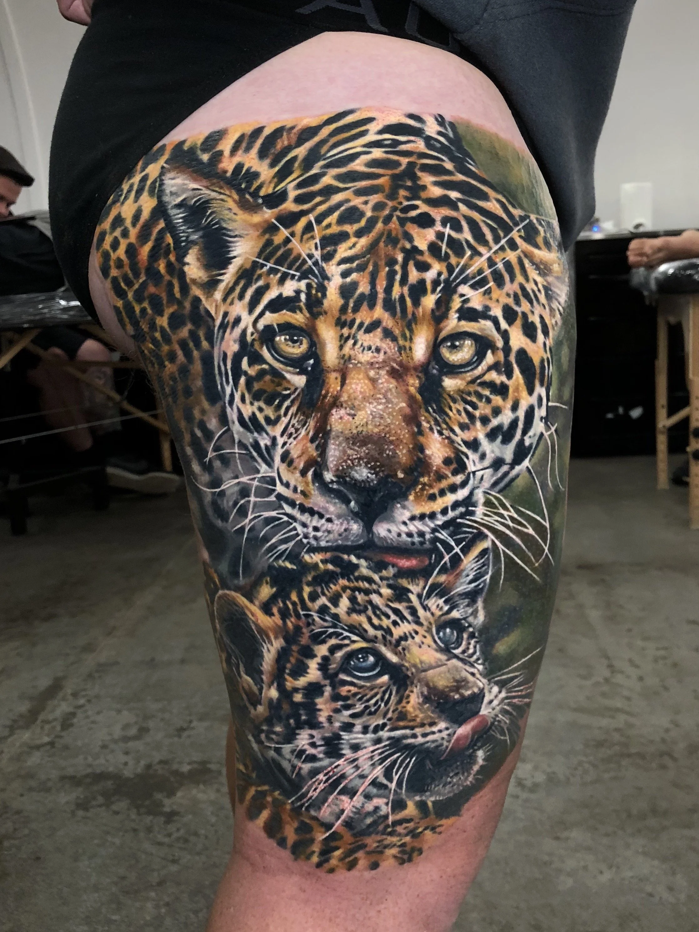 Tattoo of a jaguar's face on a person's thigh, showing the detailed features of the jaguar's face including eyes, nose, and fur pattern.