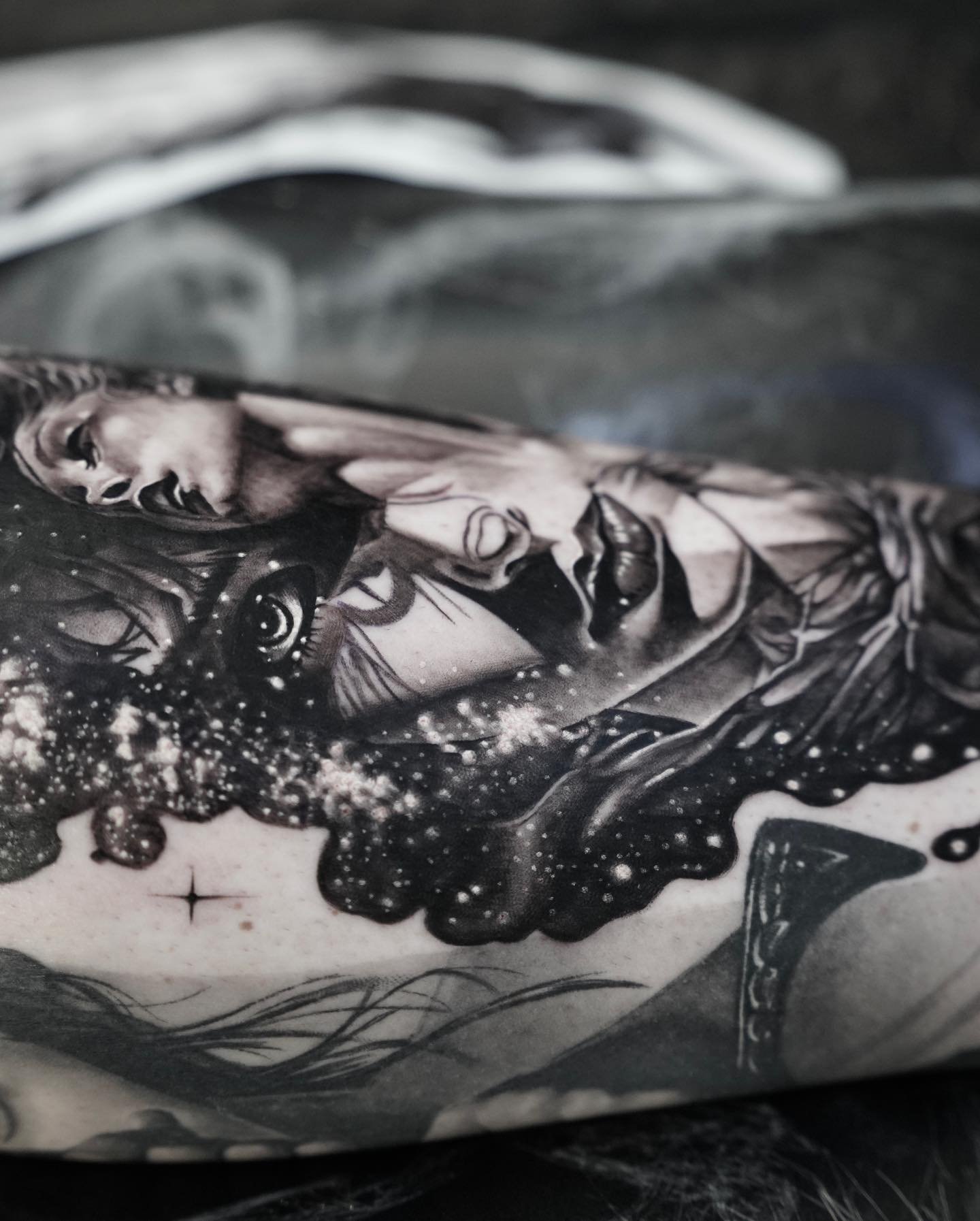 Black and white tattoo art on a person's skin featuring a woman's face surrounded by abstract and cosmic elements.