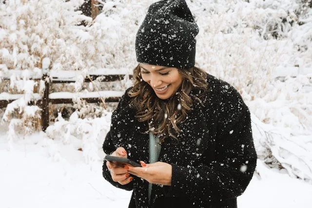 woman-in-black-knit-cap-and-black-coat-holding-black-smartphone