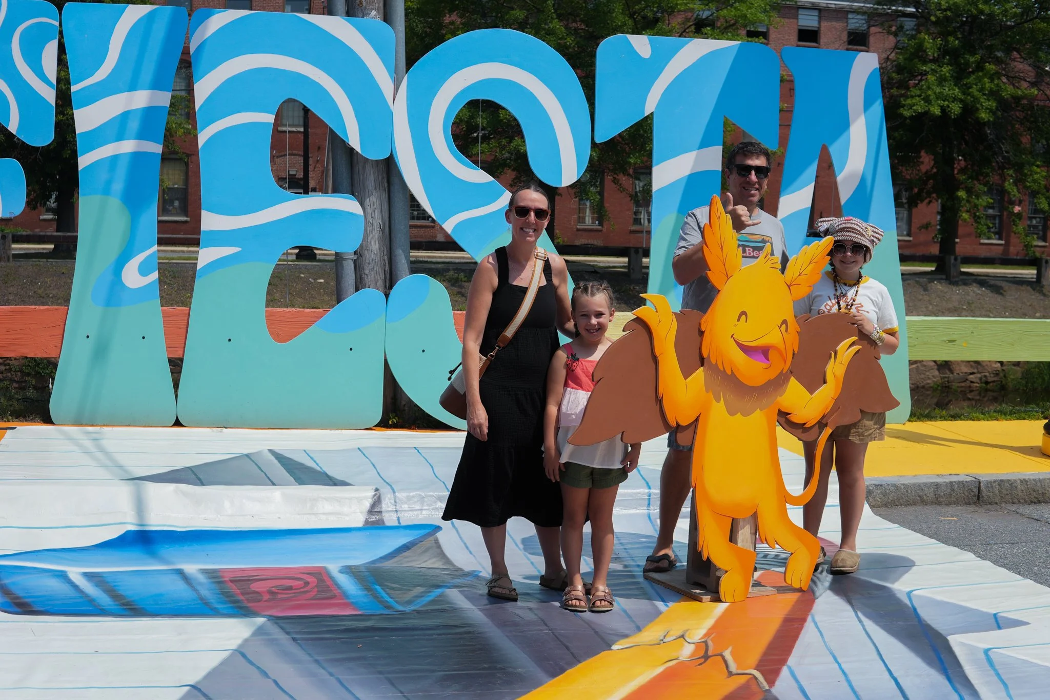 Family group standing outdoors in front of colorful sign and a cartoon lion figure.