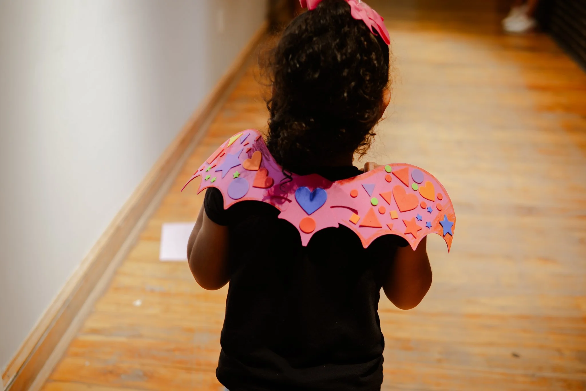 Child wearing a pink, star-decorated cape walking down a wooden hallway.