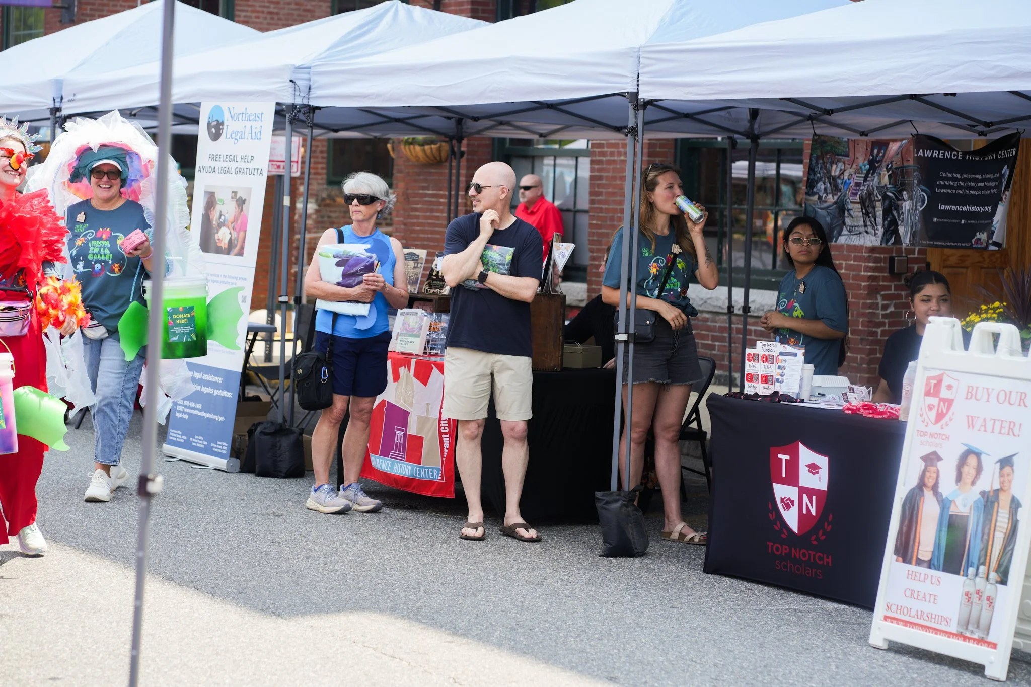 People attending an outdoor community event with booths and tables promoting local organizations and scholarships.